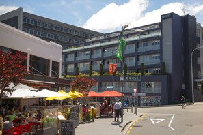 A modern building with a sign reading "QUEST" and a street-level café with outdoor seating.
