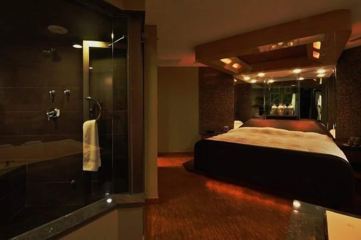 Une chambre d’hôtel moderne avec un grand lit, une douche en verre et un miroir qui reflète la pièce.