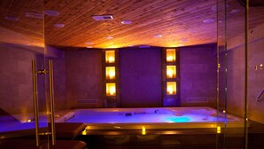 A spa room with a wooden ceiling, a large hot tub, and glass walls.