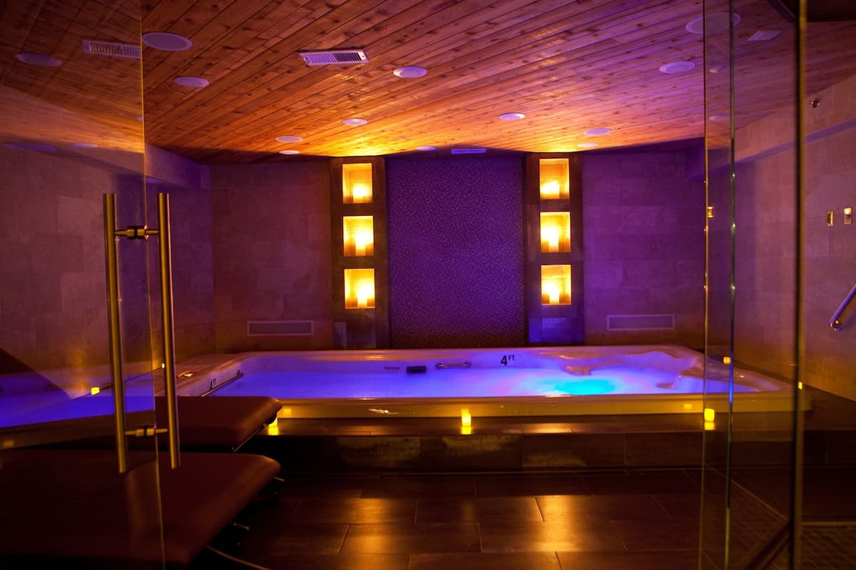 Une salle de spa avec un plafond en bois, un grand jacuzzi et des murs en verre.