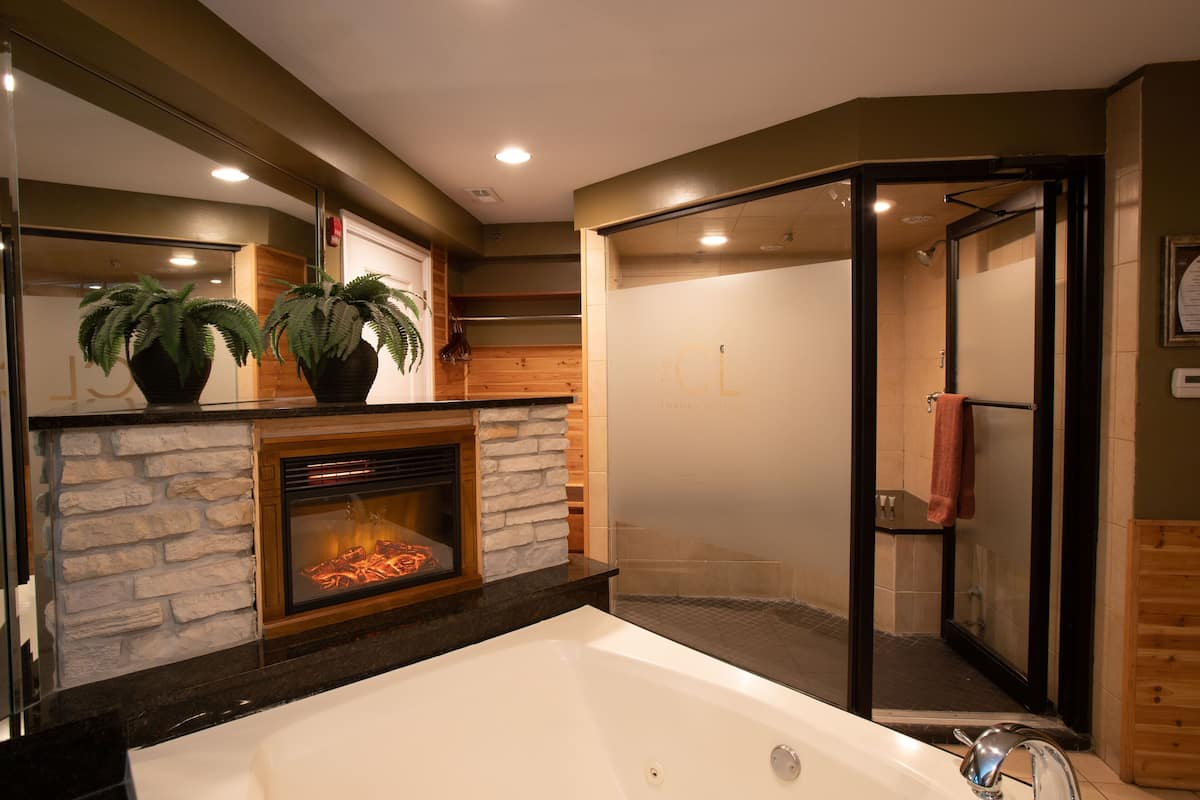 Une salle de bain moderne dotée d’une grande baignoire, d’une douche en verre et d’une cheminée agrémentée de deux plantes en pot.