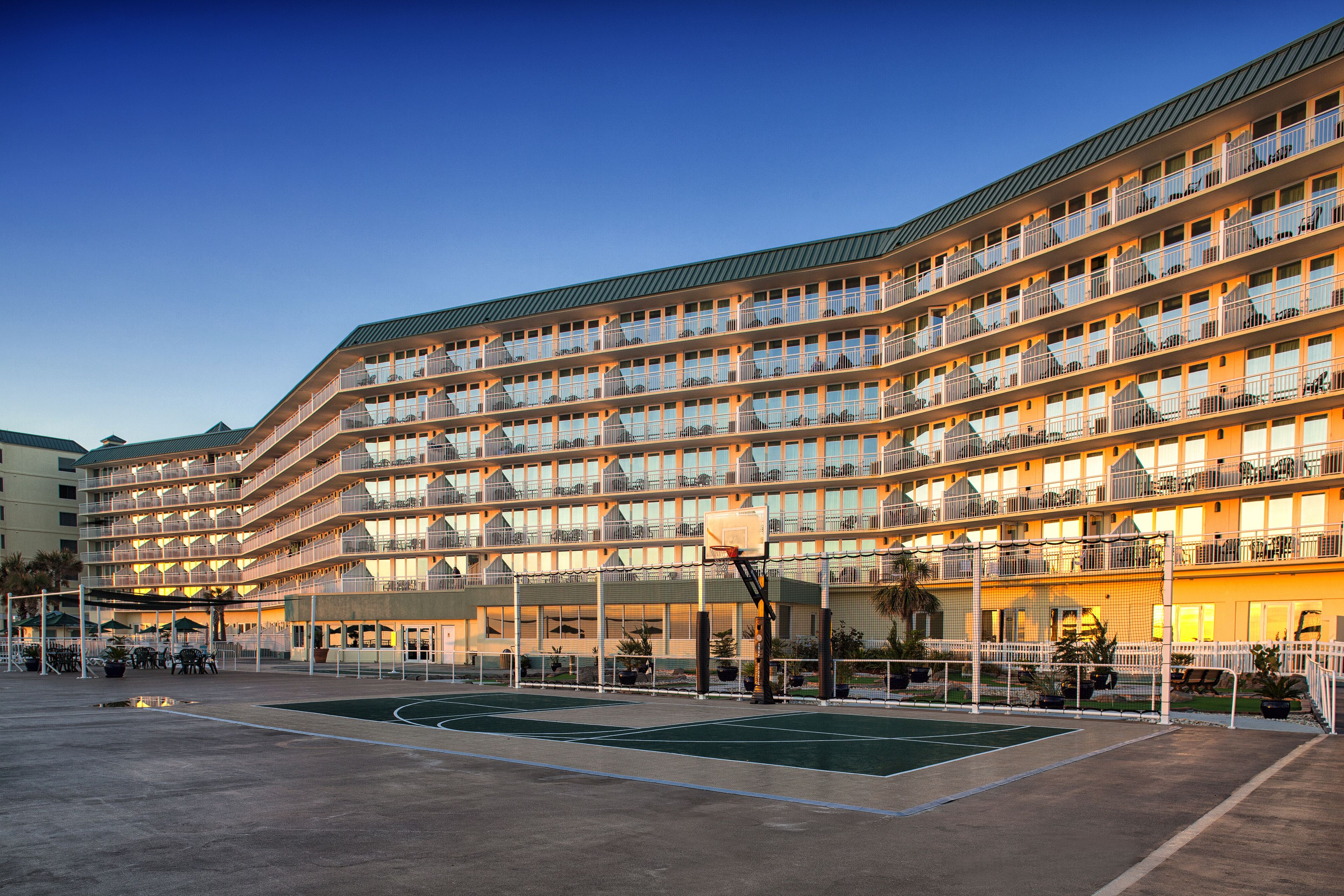 Een hotel met meerdere verdiepingen, balkons, een basketbalveld en buiten zitplekken.