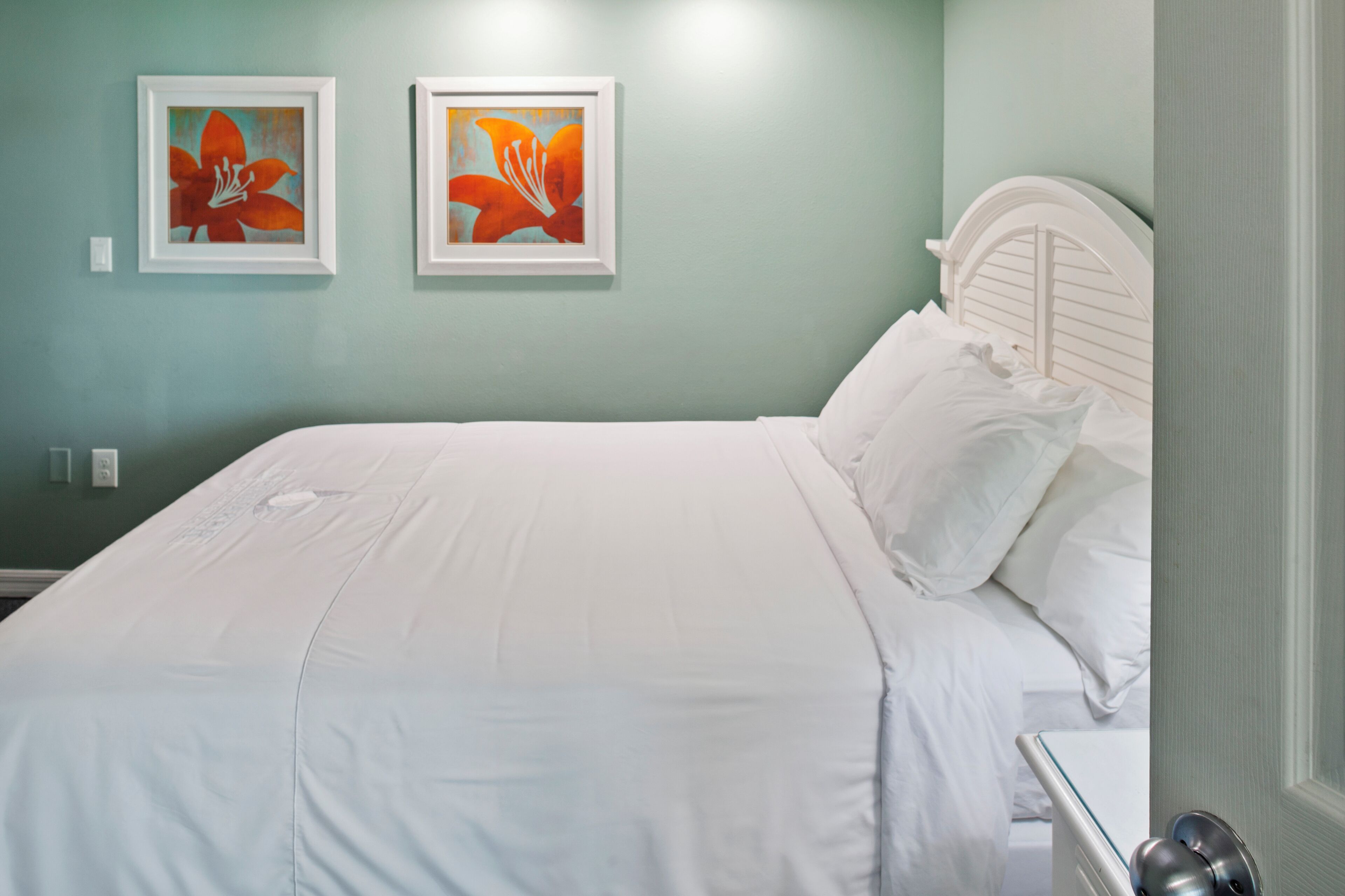 Un lit bien fait, avec du linge de lit blanc, dans une pièce aux murs de couleur turquoise.