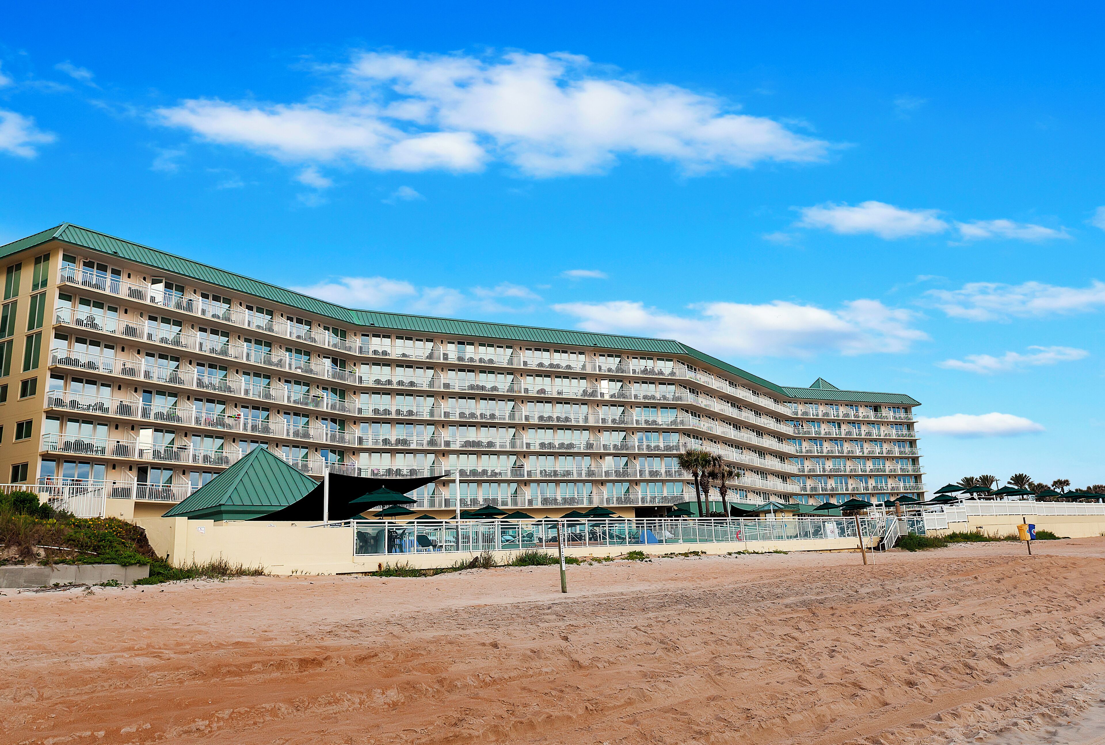 Un hotel grande de varios pisos con balcones, situado cerca de una playa de arena.