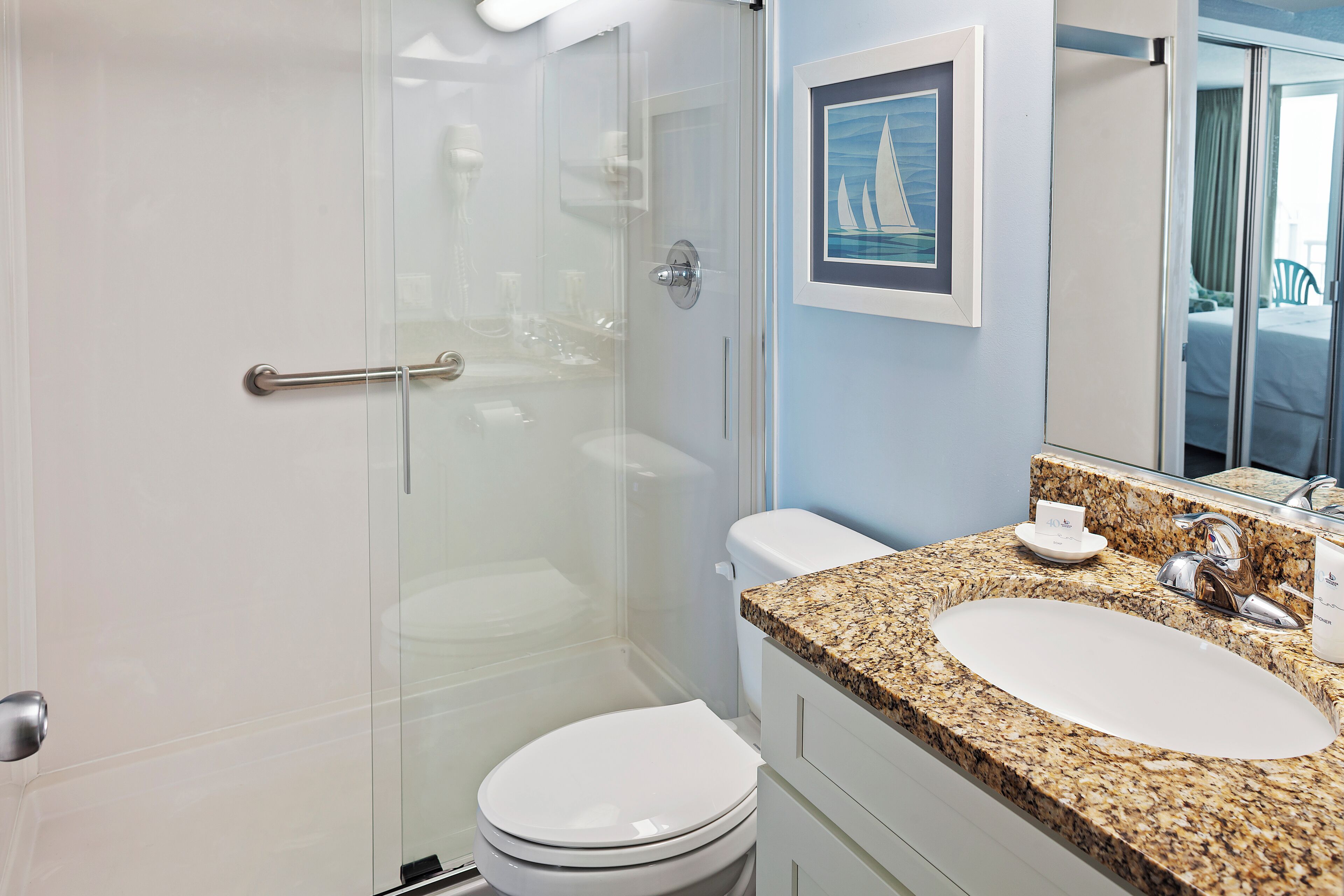Un baño moderno con cabina de ducha de vidrio, inodoro blanco y encimera de granito con lavabo y tocador.