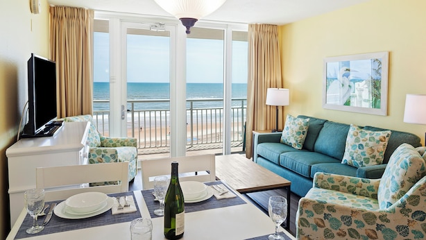 Habitación de hotel con zona de comedor, sofá y vista a la playa.