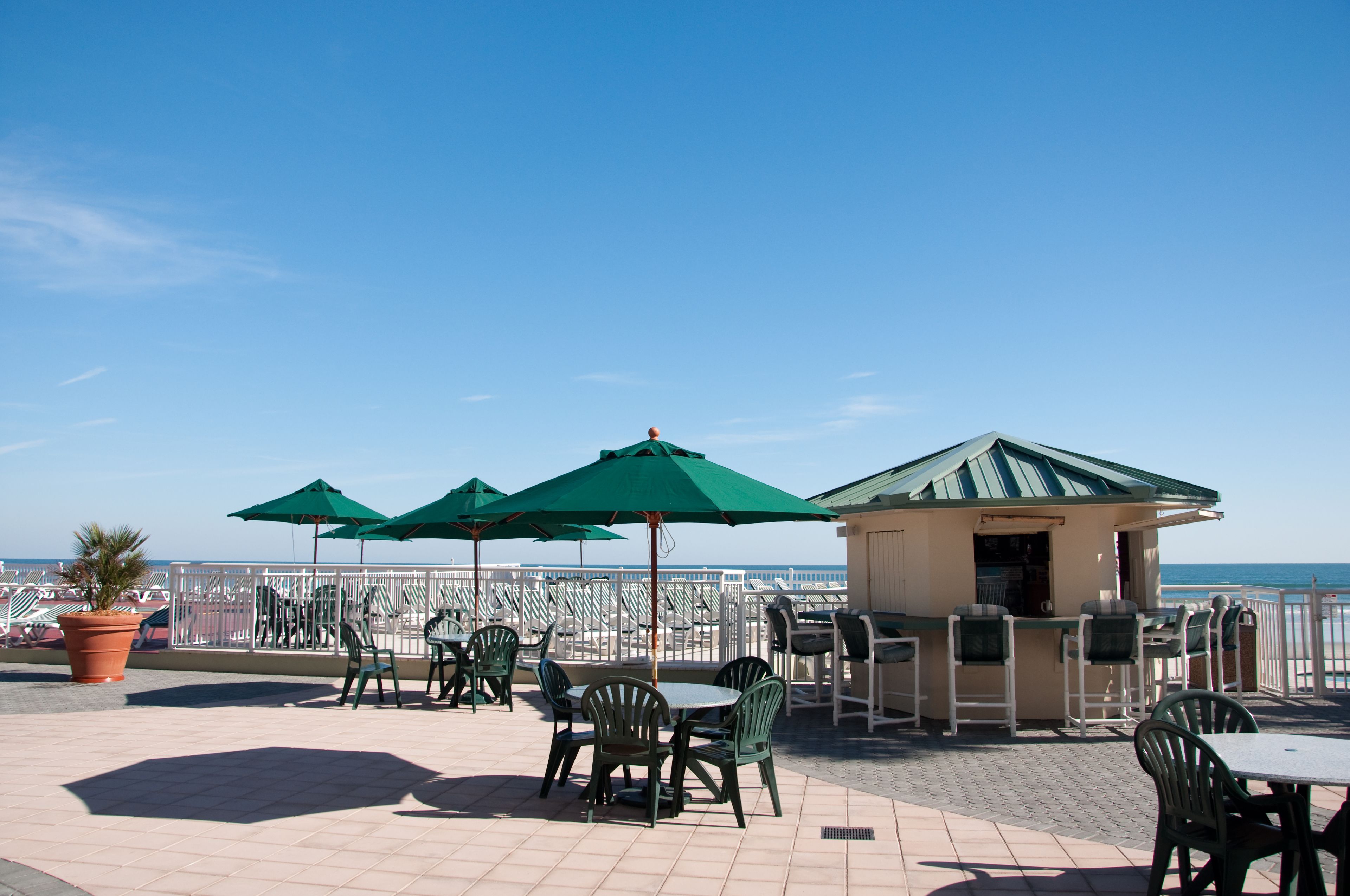 An outdoor patio with green chairs and umbrellas, a small bar area, and a view of the sea.