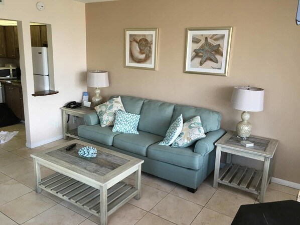 A living room with a light blue sofa, two side tables with lamps, a coffee table, and two framed pictures on the wall.