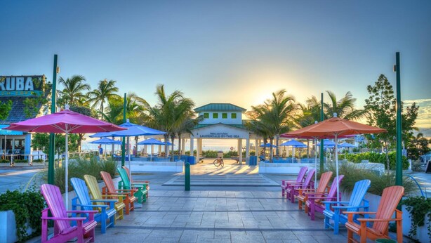 A beachfront area with colorful Adirondack chairs and umbrellas, a sign for 'LAUDERDALE-BY-THE-SEA', and palm trees. - Sea Cliff Motel (Lauderdale-by-the-Sea)
