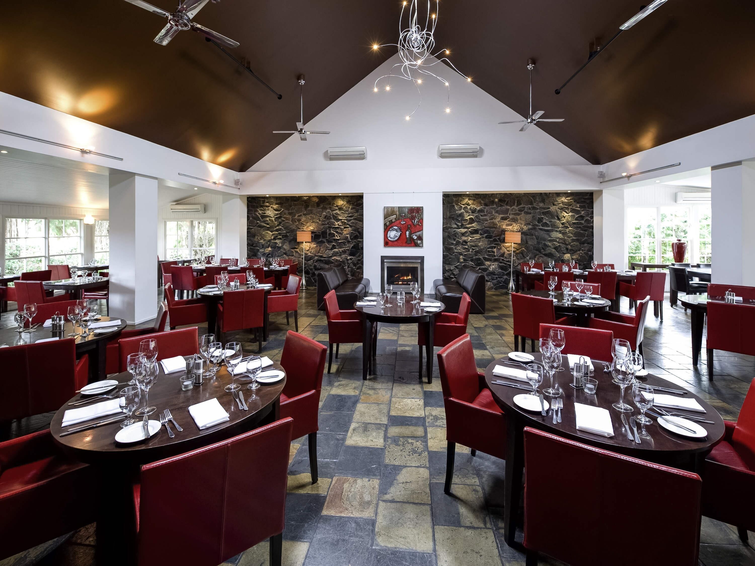 Un restaurante espacioso con varias áreas de comedor, sillas tapizadas en rojo y una pared de piedra con chimenea.