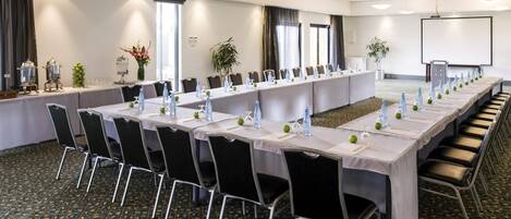 Een vergaderzaal met een lange tafel, stoelen en een projectiescherm.