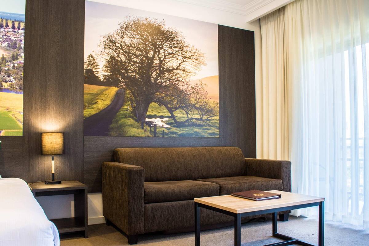 A room with a sofa, a small table, a lamp, and a large painting of a tree.