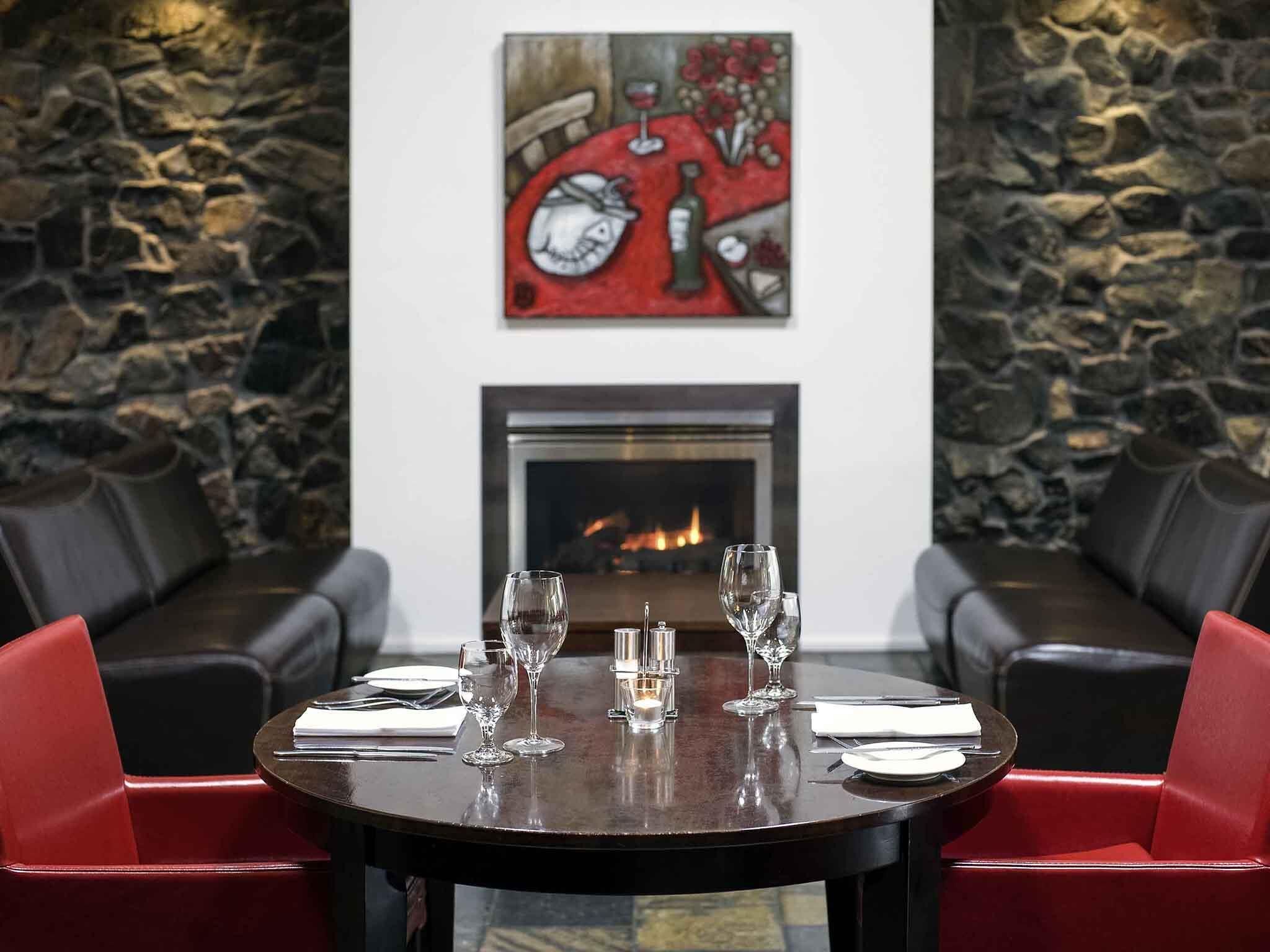 A dining area with a fireplace, stone walls, and red upholstered seating.
