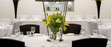 Ein Esstisch, gedeckt mit weißen Tischdecken, Stühlen und einer Vase mit gelben Blumen.