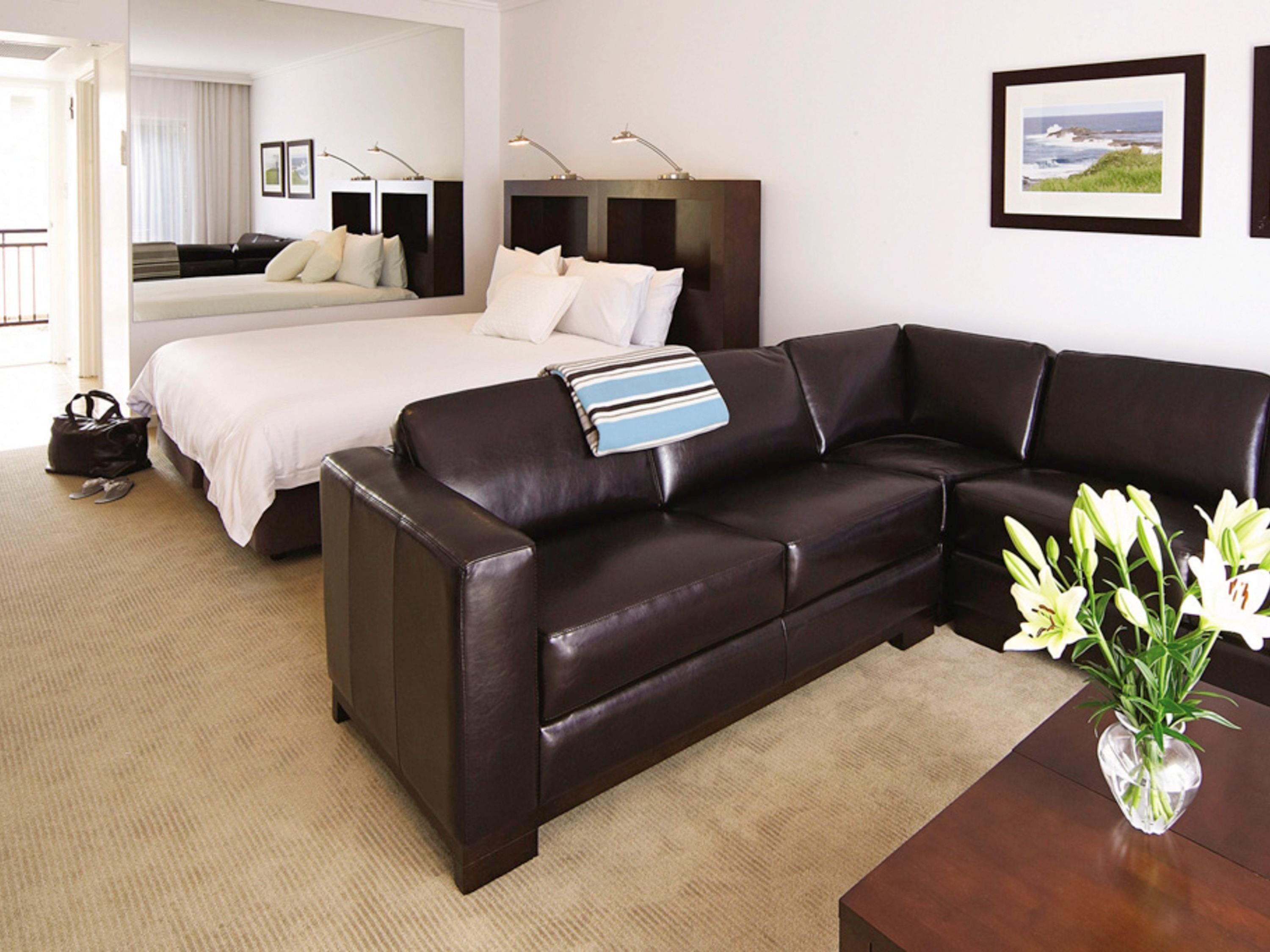 A hotel room with a bed, a sofa, a desk, and a vase of flowers.