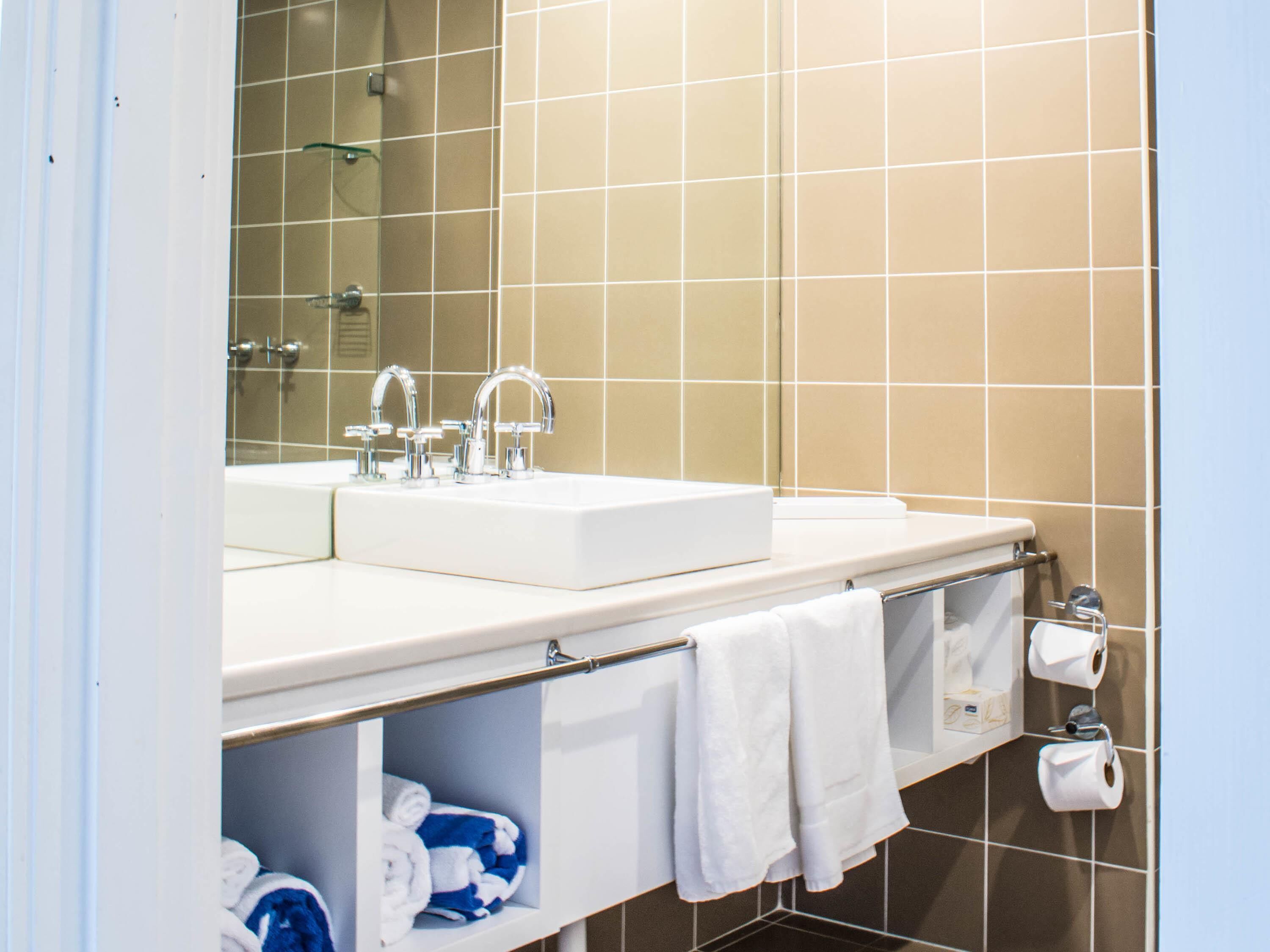 A bathroom with a white sink, two faucets, a mirror, and a towel rack with white towels.