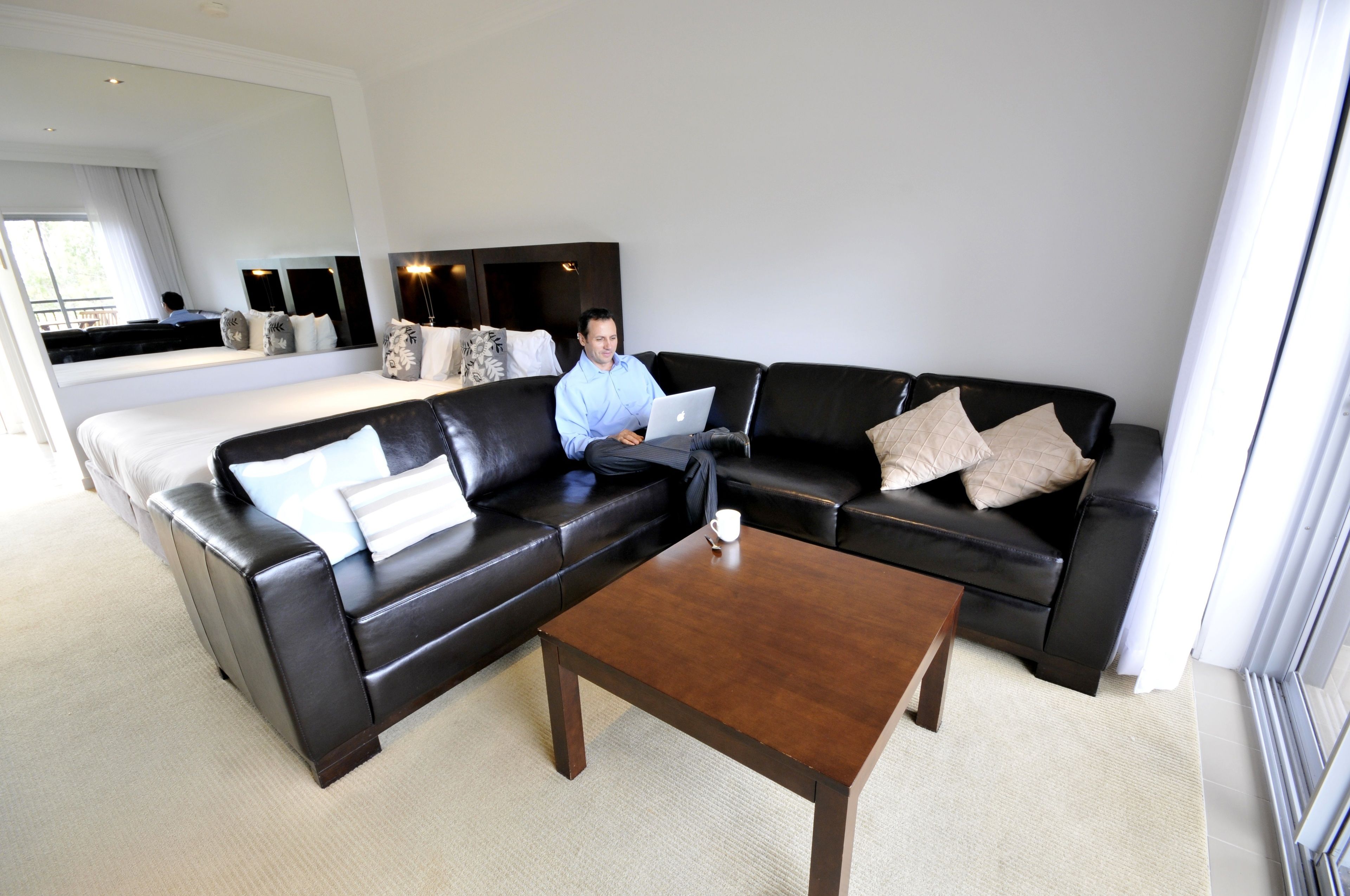 A modern living room with a black leather sofa, a wooden coffee table, and a large mirror on the wall.