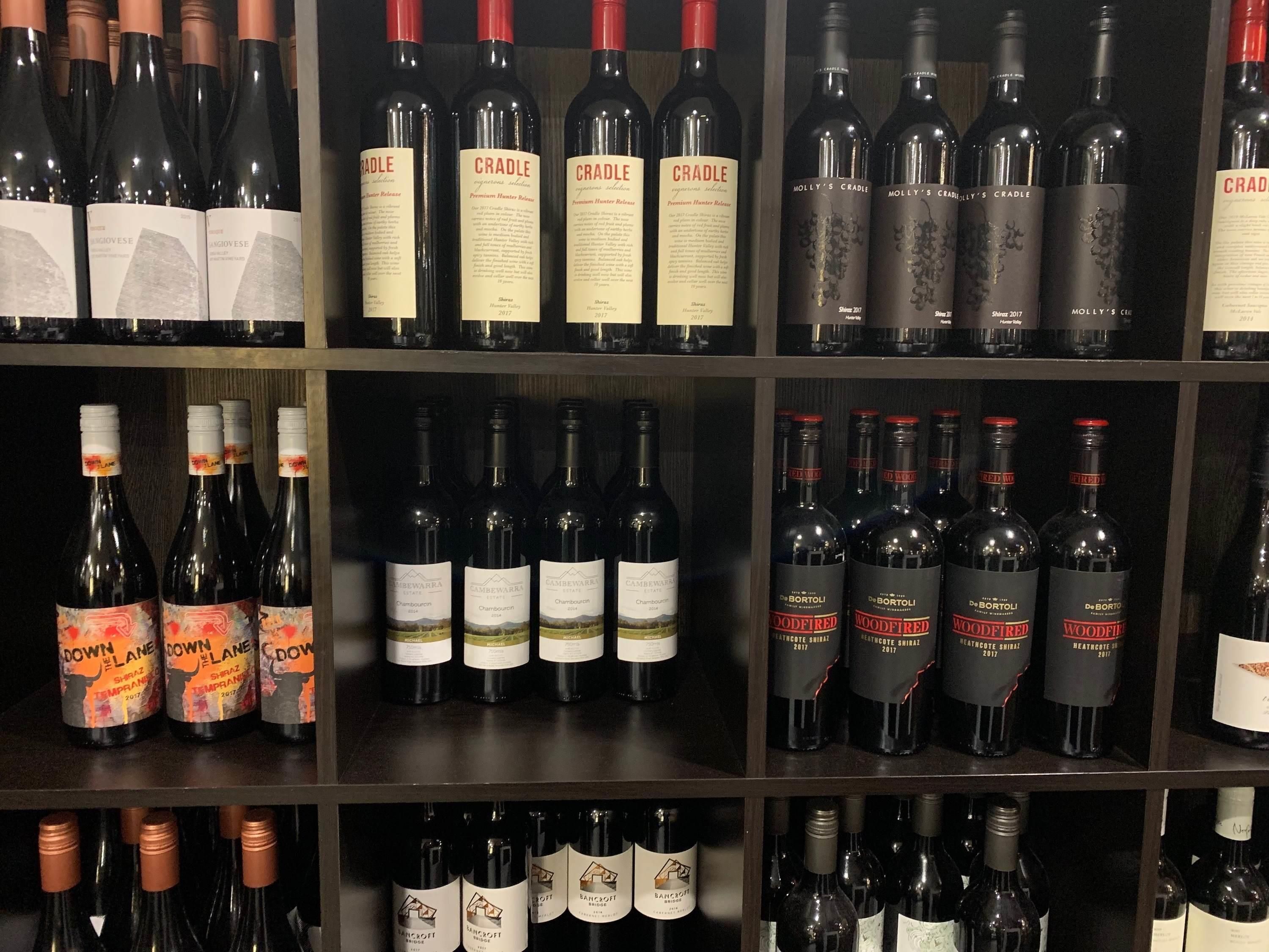 Una estantería para vinos con varias botellas, incluyendo marcas como Cradle y Woodfired.