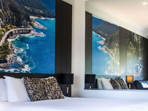 Habitación de hotel con una cama grande, una mesita de noche, una lámpara y una pared decorada con una fotografía panorámica.