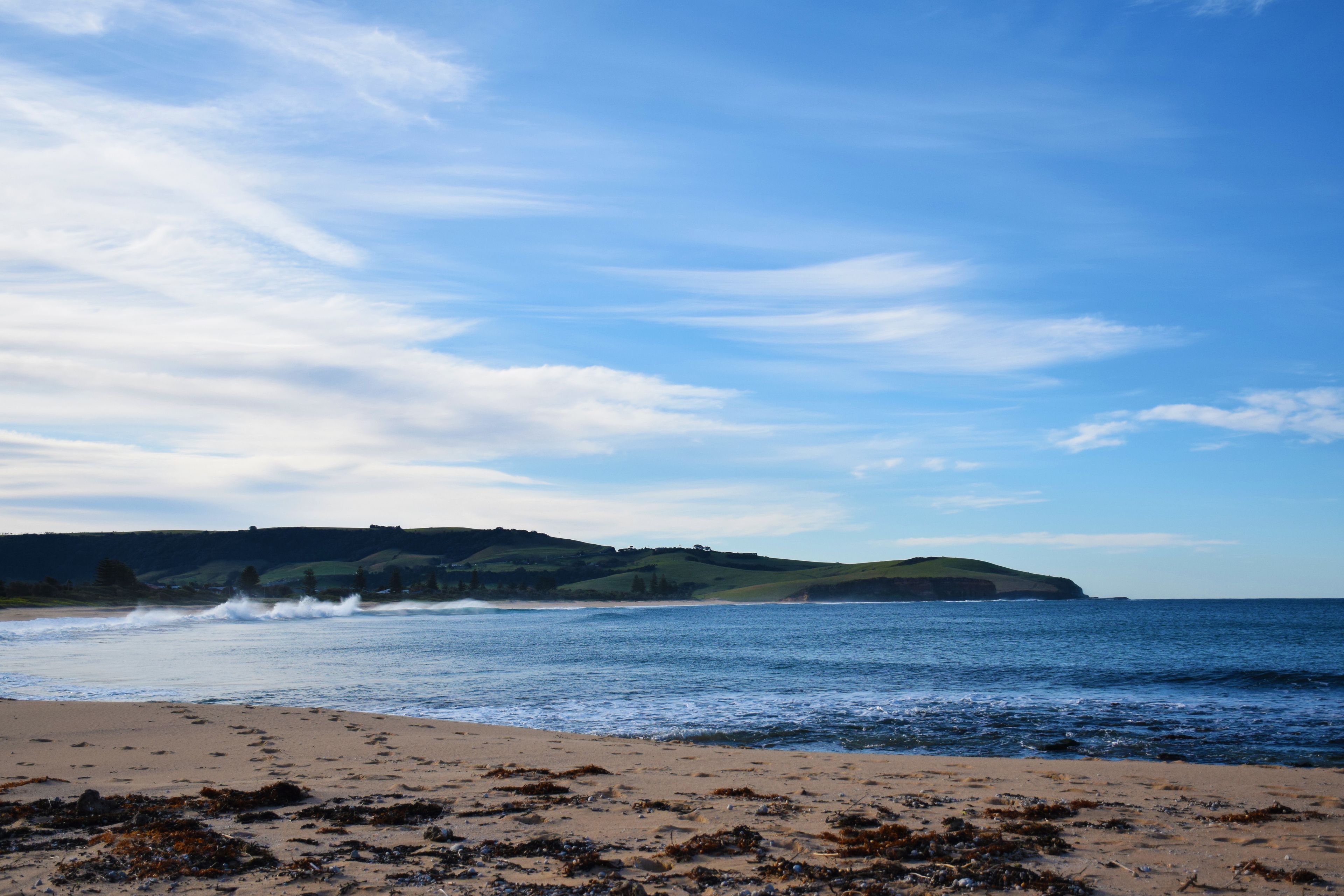A beach with waves, a clear sky, and distant hills.