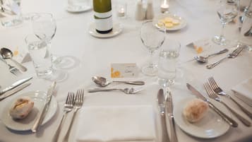 Una mesa de comedor formal dispuesta con varios vasos de vino, tenedores, cuchillos y cucharas, además de platos y una botella de vino.