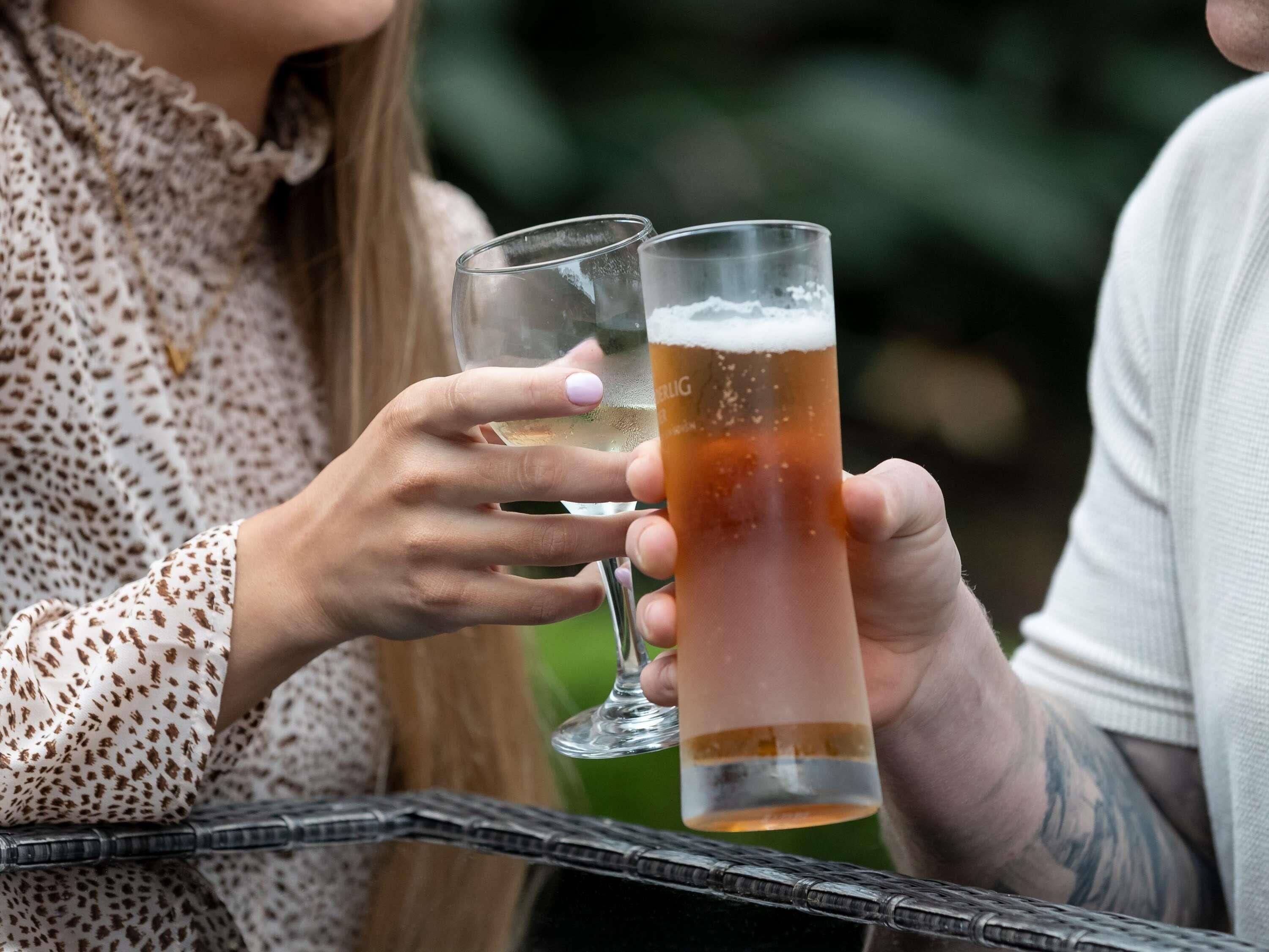 Two people holding glasses of beer, one with a clear liquid and the other with a golden liquid.