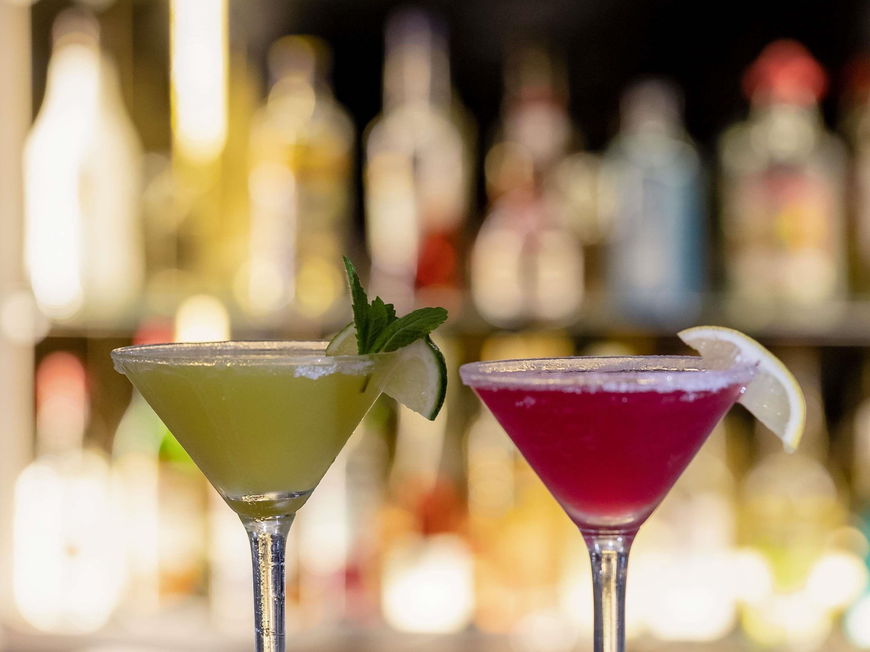 Two martini glasses with a blurred background of bar bottles.