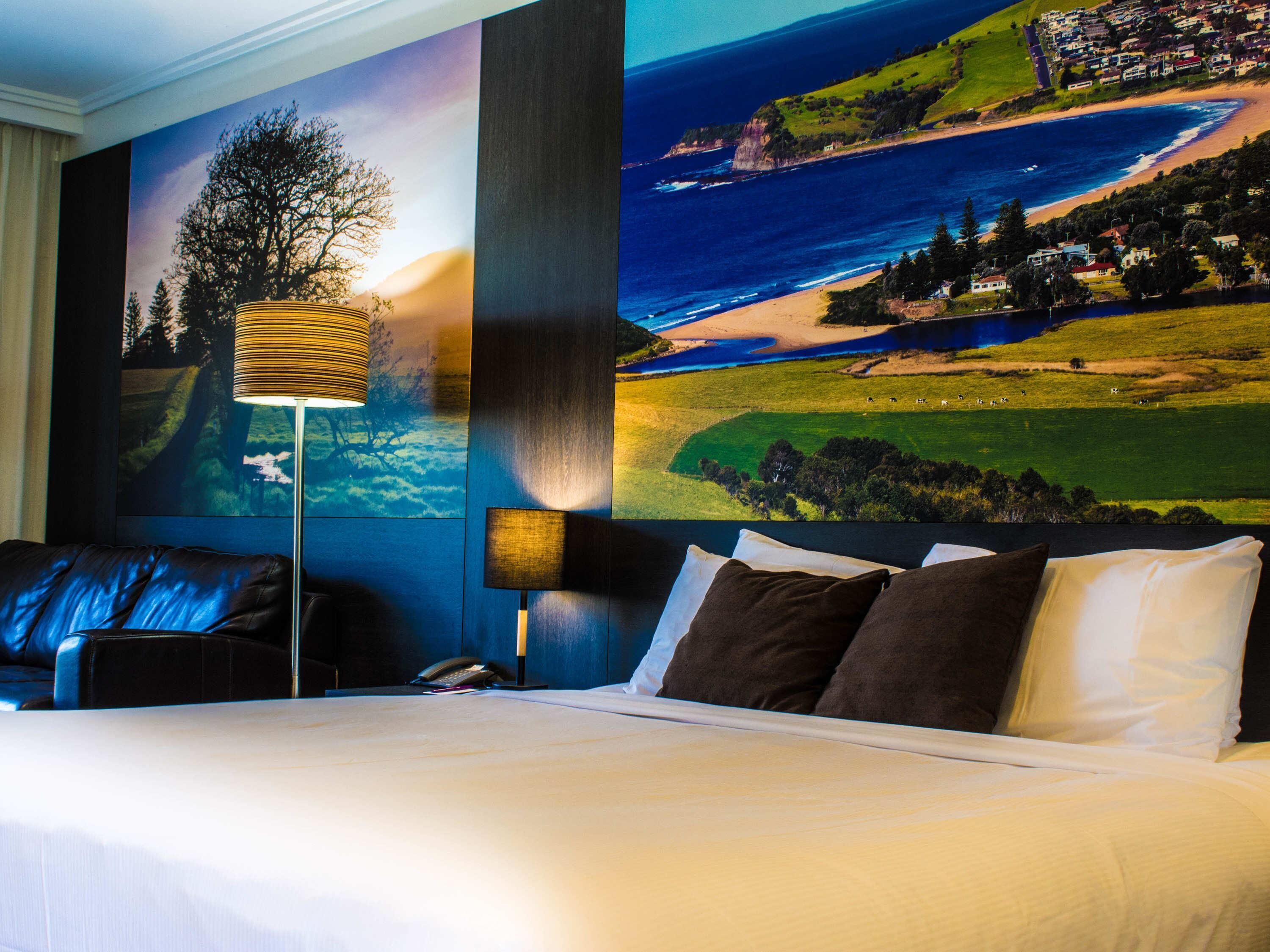 A hotel room with a bed, two bedside lamps, a telephone, and a large scenic wall mural.