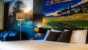 A hotel room with a bed, two bedside lamps, a telephone, and a large scenic wall mural.