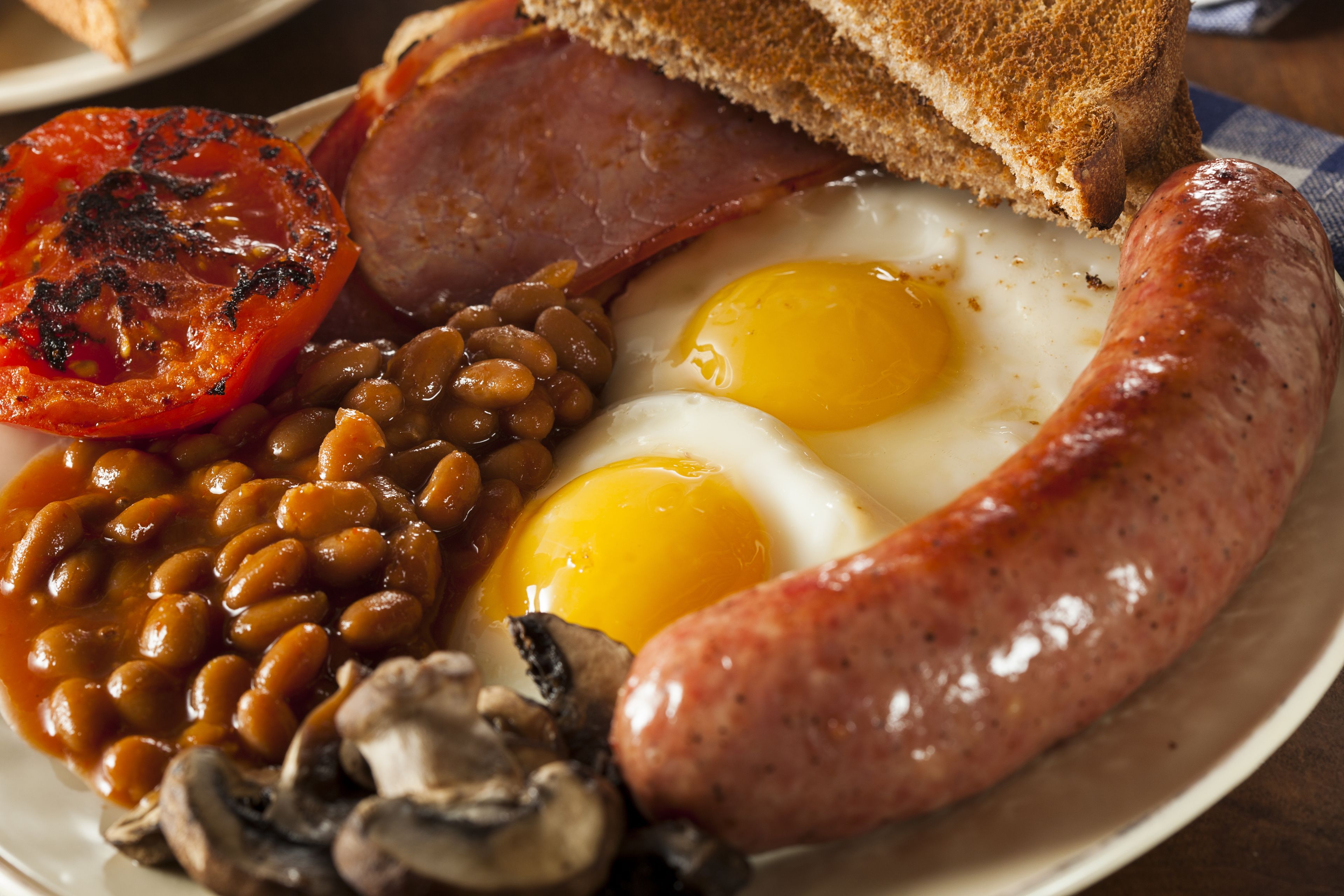 A plate of breakfast food including eggs, sausage, beans, and a grilled tomato.