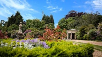 A garden with a gazebo, lush greenery, and a statue.