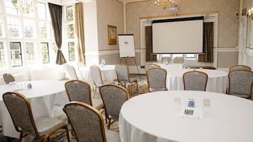A conference room with round tables, grey upholstered chairs, a projector screen, and a whiteboard.