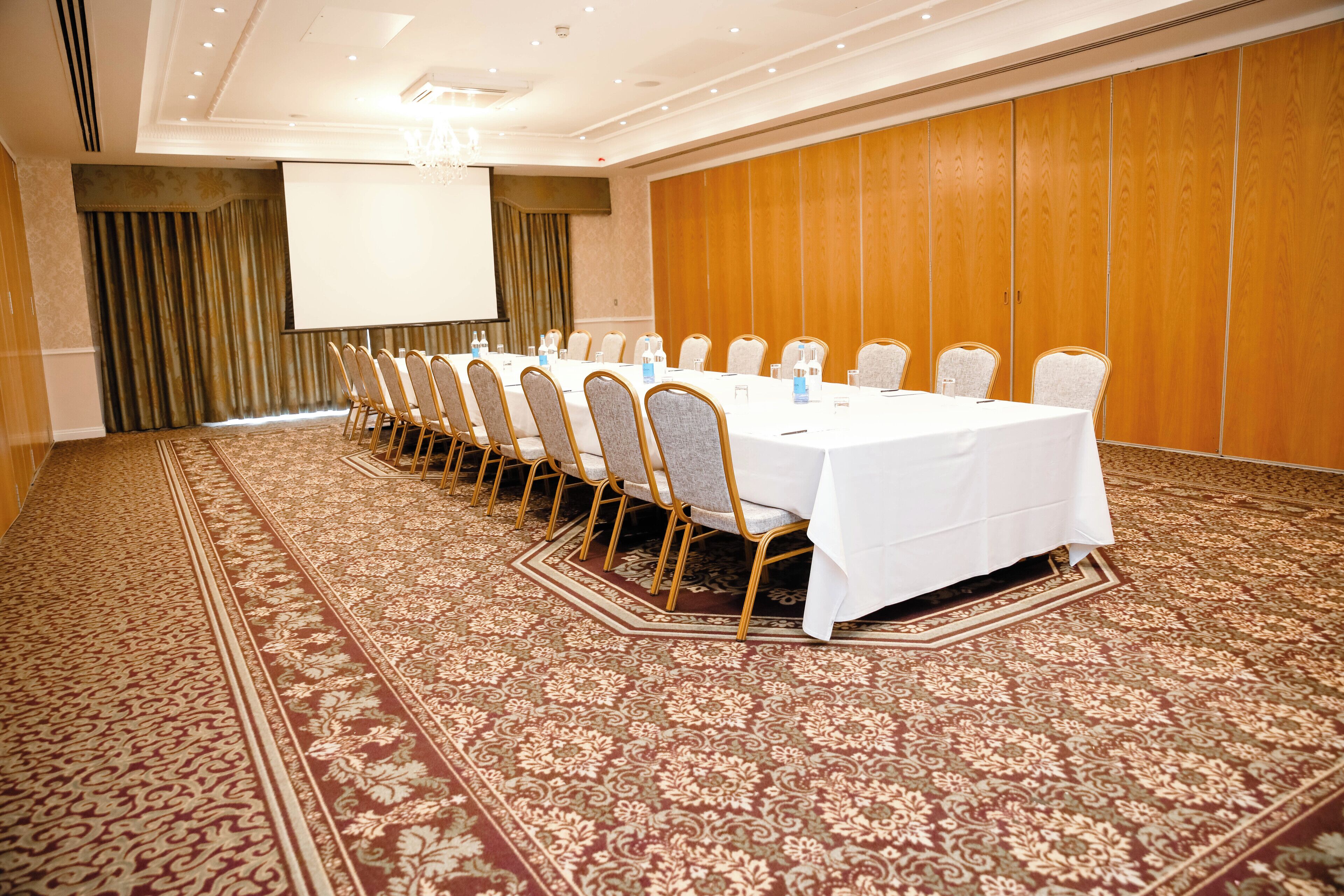 Une salle de conférence avec une longue table, des chaises, un écran de projection et une moquette à motifs.