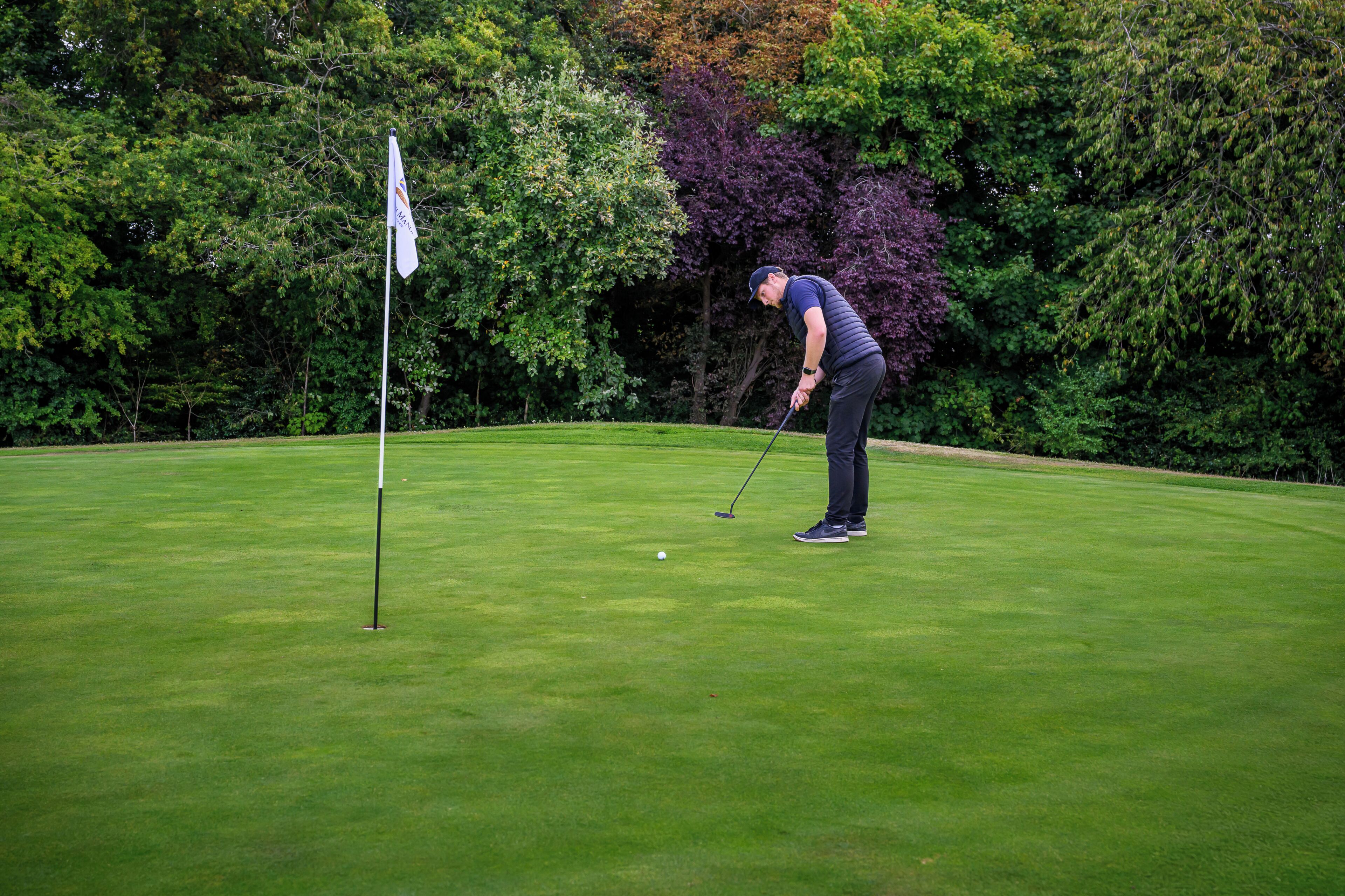 A golf course with a flagstick, a golfer in a cap and vest, and a well-maintained green.
