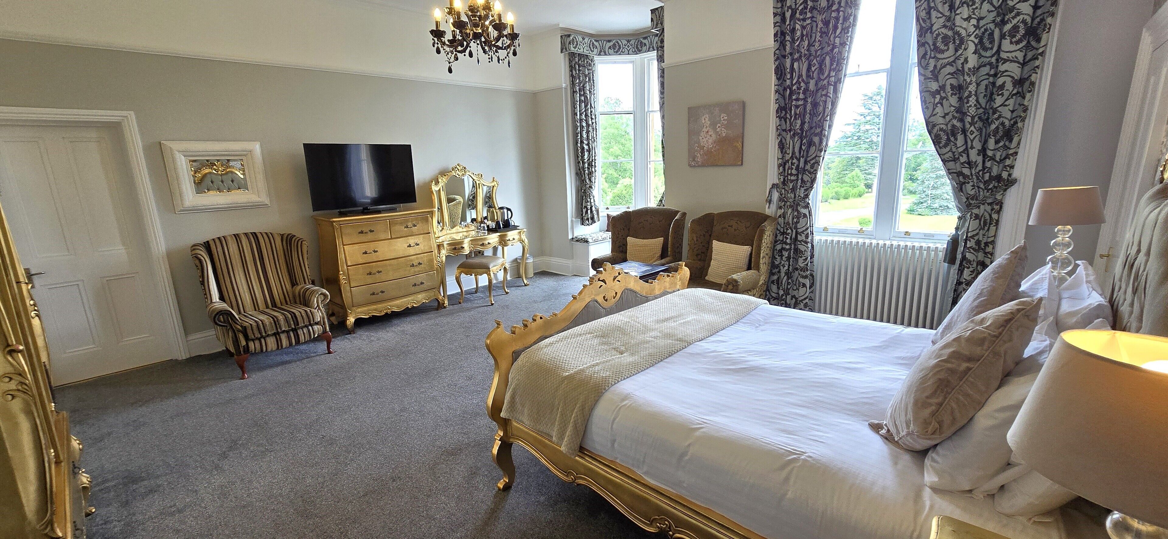 A spacious bedroom with a large bed, a dresser, a television, and two armchairs.