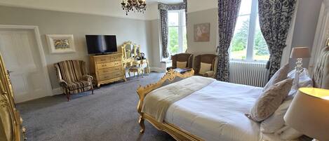 A spacious bedroom with a large bed, a dresser, a television, and two armchairs.