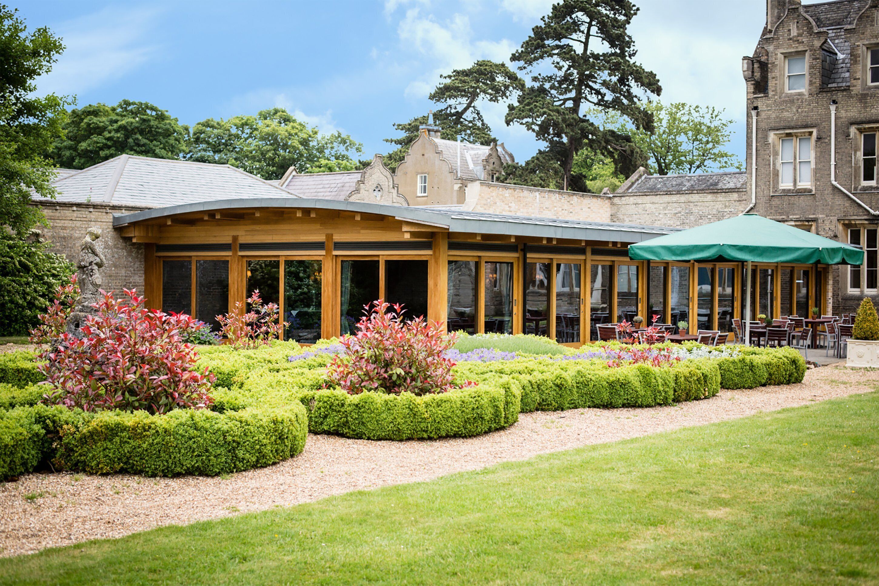 A building with a covered patio area, surrounded by well-manicured gardens and a lawn.