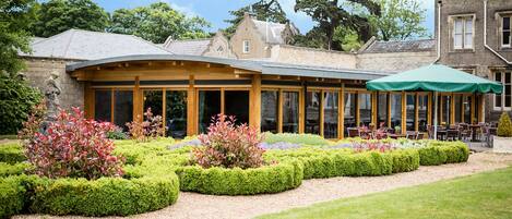 A building with a covered patio area, surrounded by well-manicured gardens and a lawn.