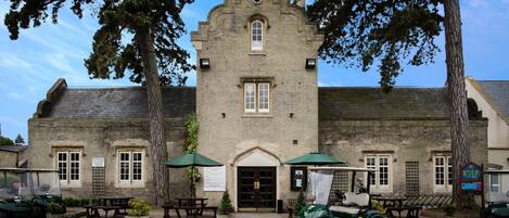 A historic building with a central entrance, two green umbrellas, and a golf cart in front.