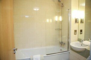 Un baño con bañera, ducha con mampara de vidrio y lavamanos.