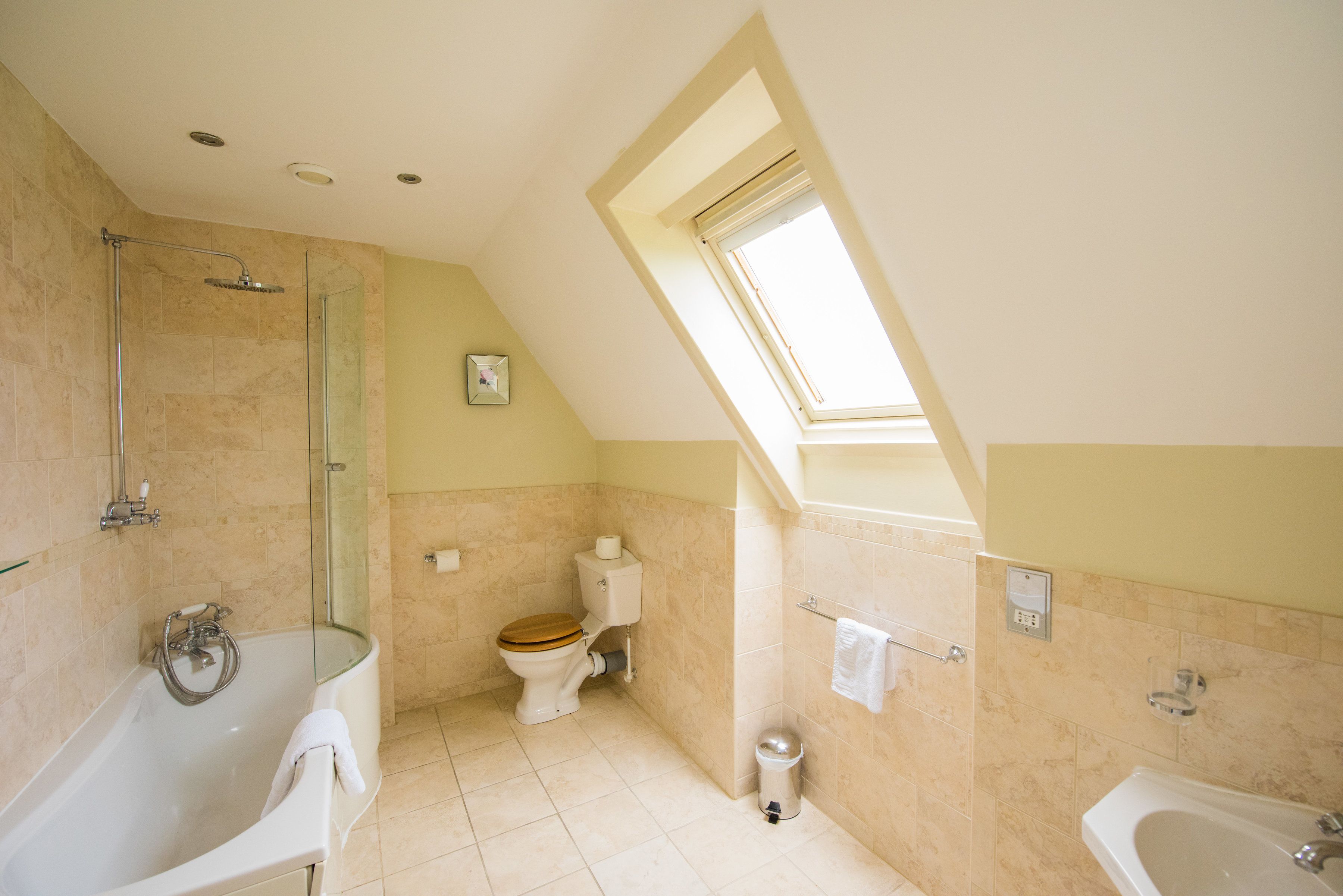 A bathroom with a skylight, a bathtub, a toilet, and a shower area.