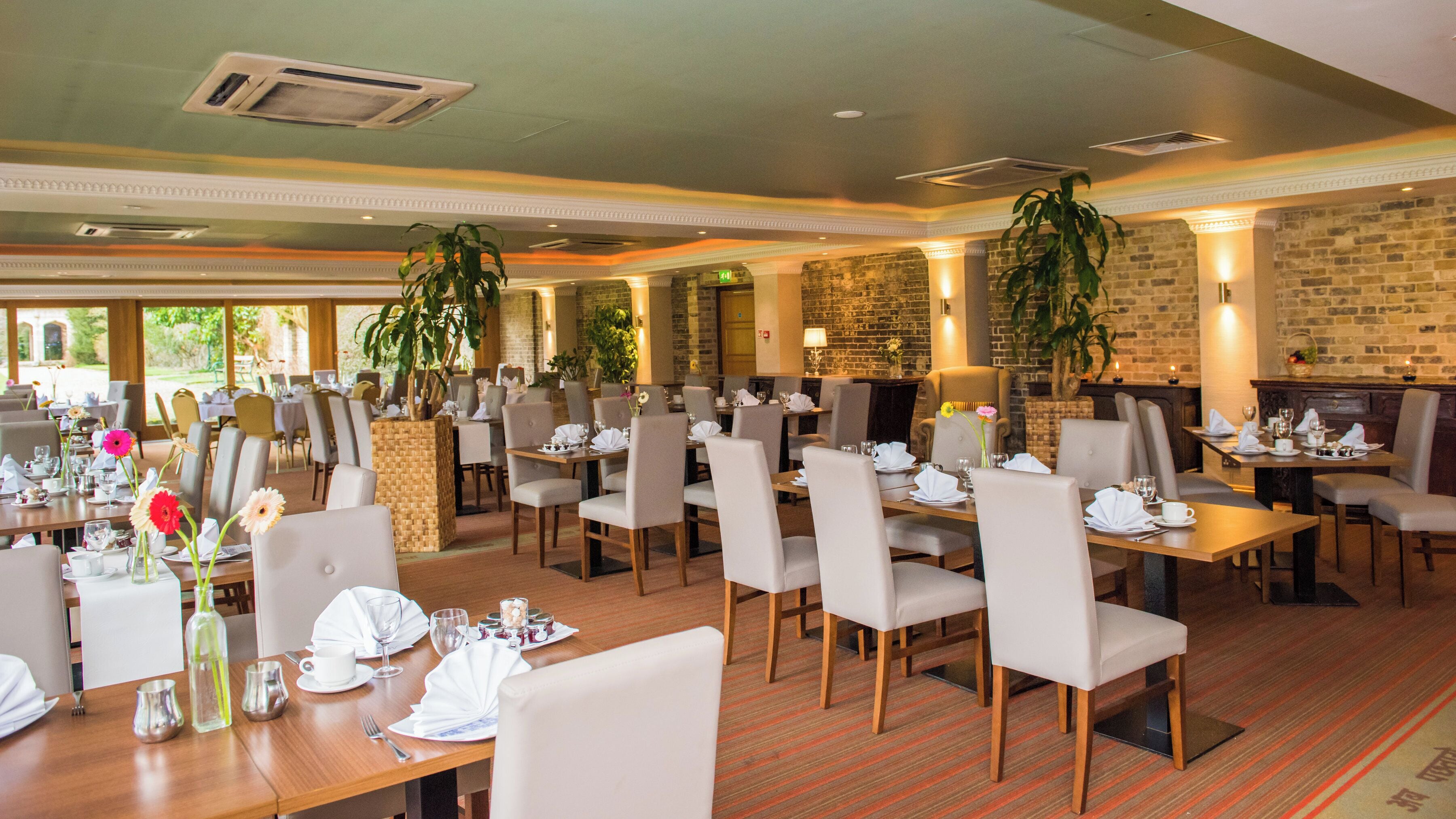 Un comedor espacioso con varias mesas dispuestas para los comensales, con una combinación de luz natural y artificial, y un fondo de pared de ladrillo.