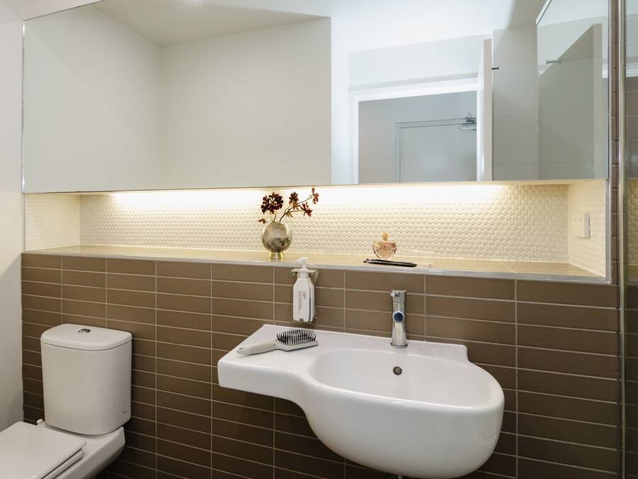 Une salle de bain avec un lavabo blanc, un miroir au-dessus et des toilettes sur la gauche.
