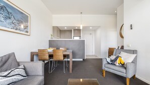 Un salon moderne avec un canapé gris, une table à manger entourée de chaises en bois, et une cuisine en arrière-plan.