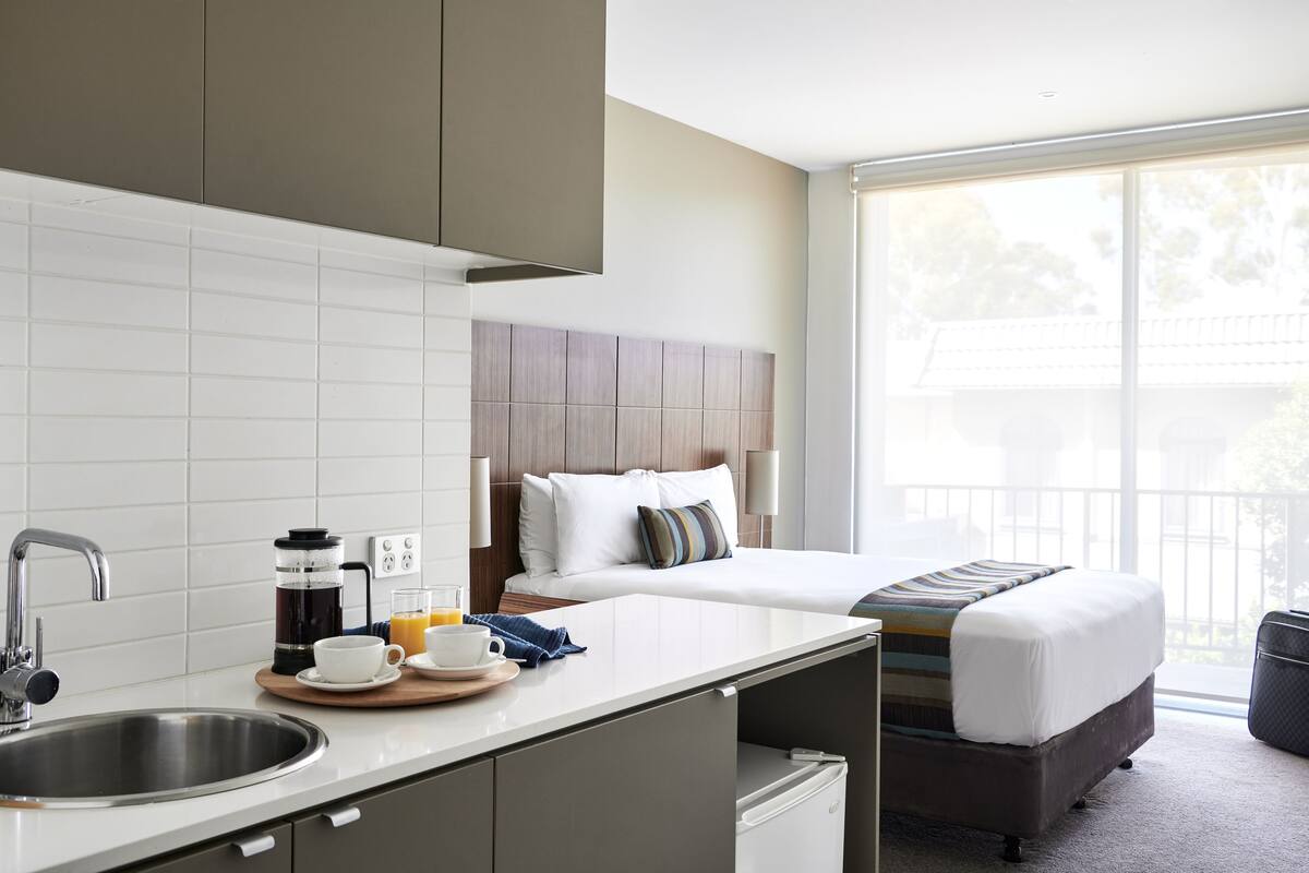 Una habitación de hotel moderna con kitchenette, cama con vistas y balcón.