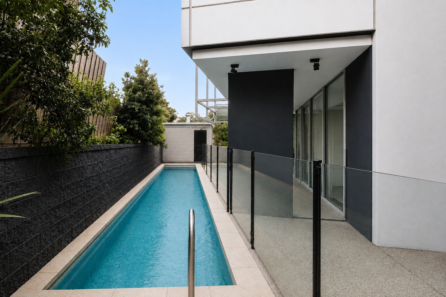 A modern building with a swimming pool, glass doors, and a black fence.
