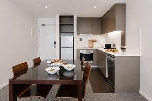 A modern kitchen with a dining area, including a glass-top table, chairs, and a built-in oven. - Punthill Knox (Wantirna South)