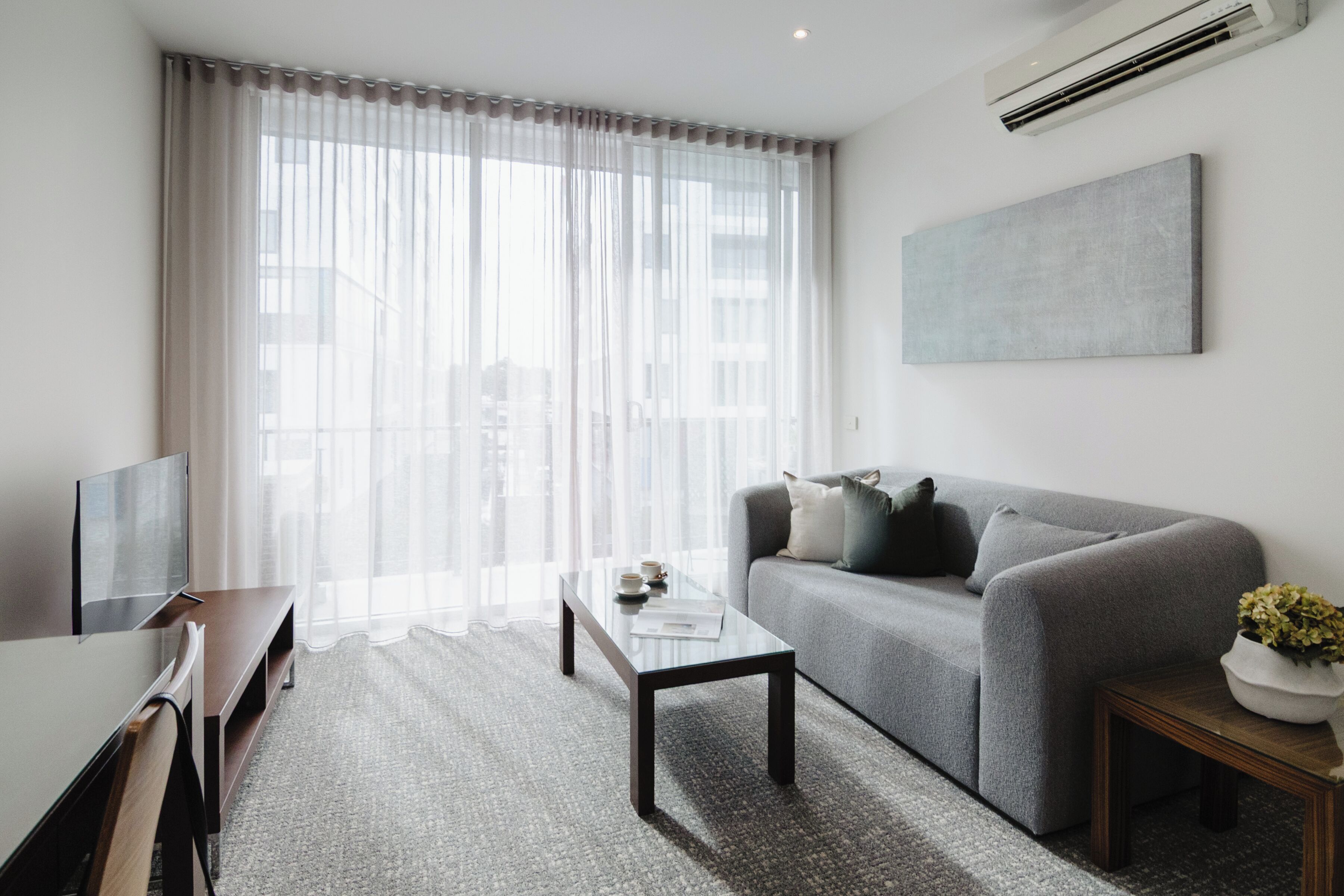 A modern living room with a grey sofa, a coffee table, and a TV on a stand.