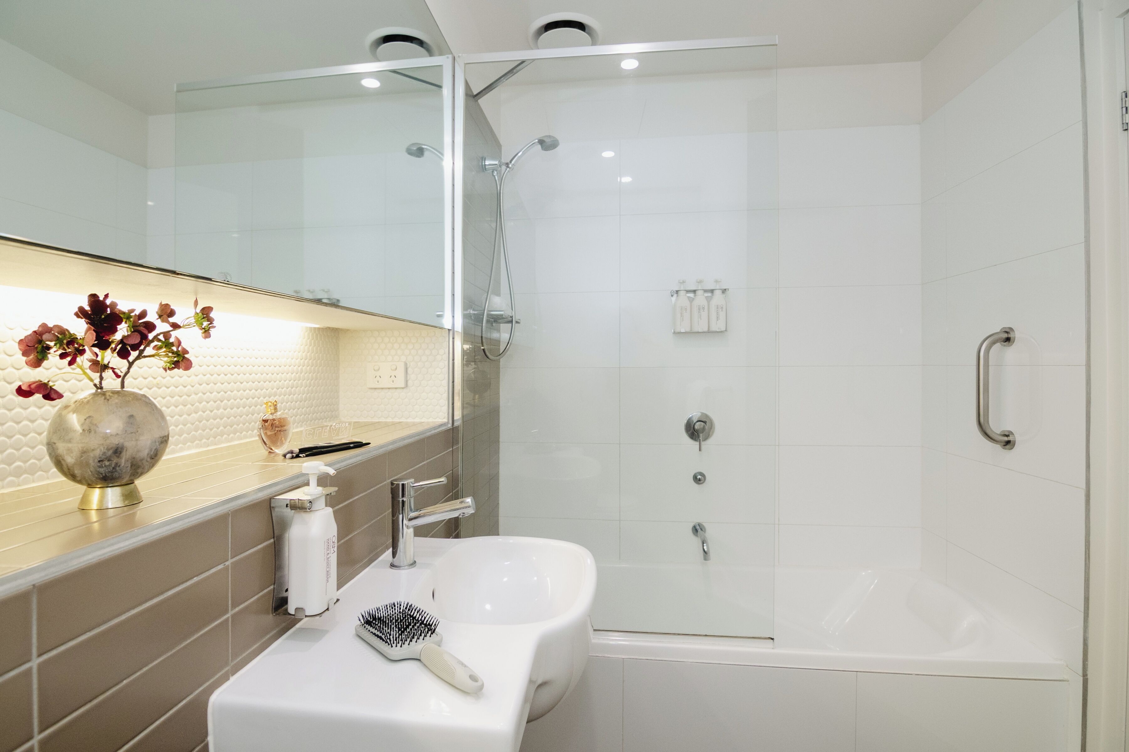 A modern bathroom with a glass shower enclosure, a white sink, and a vanity with a mirror.