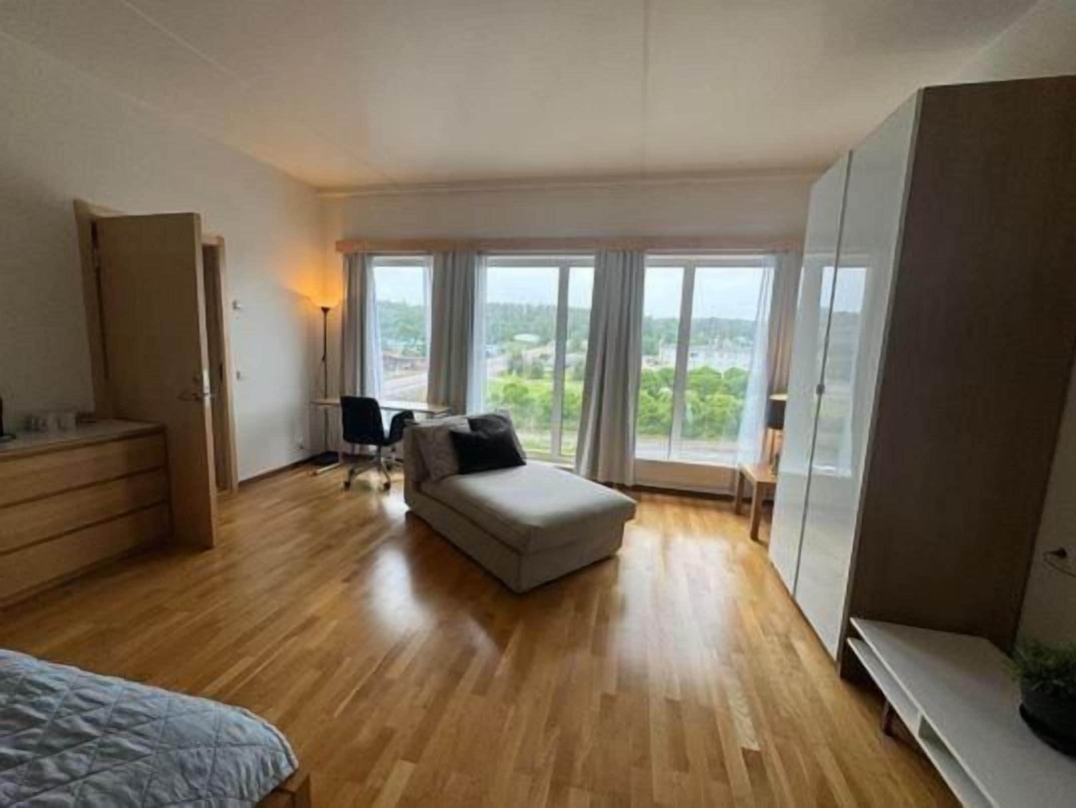 A bedroom with a bed, a sofa, a desk, and a large window with a view.